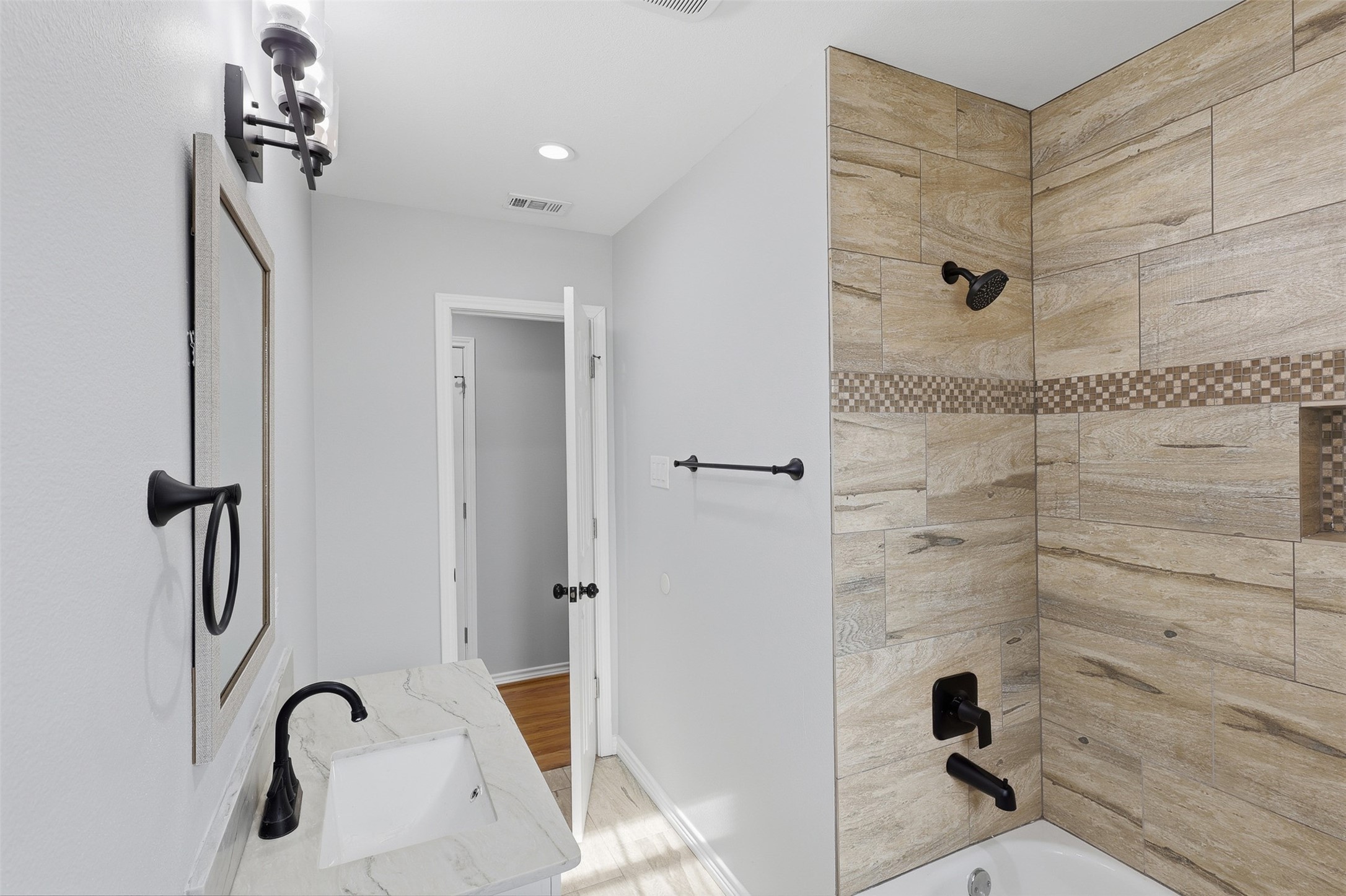 4926 Edfield Street Houston, TX 77033 - Photo 15 of 30 Bright and modern bathroom featuring a sleek vanity with a marble countertop, elegant black fixtures, and a stylish wood-look tiled shower with mosaic accents.