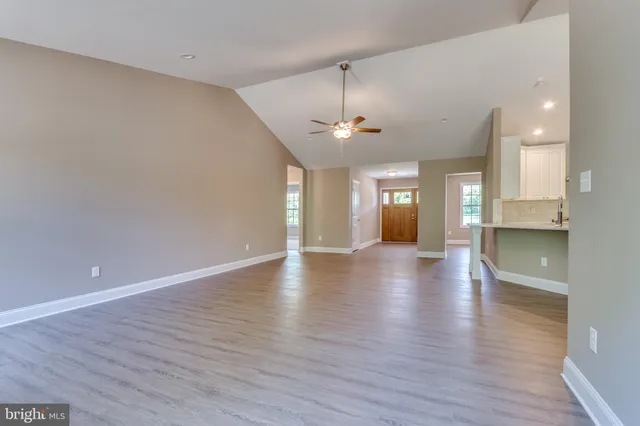 a view of an empty room and kitchen with wooden floor