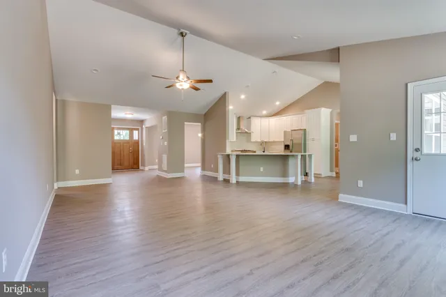 a view of an empty room and kitchen with wooden floor