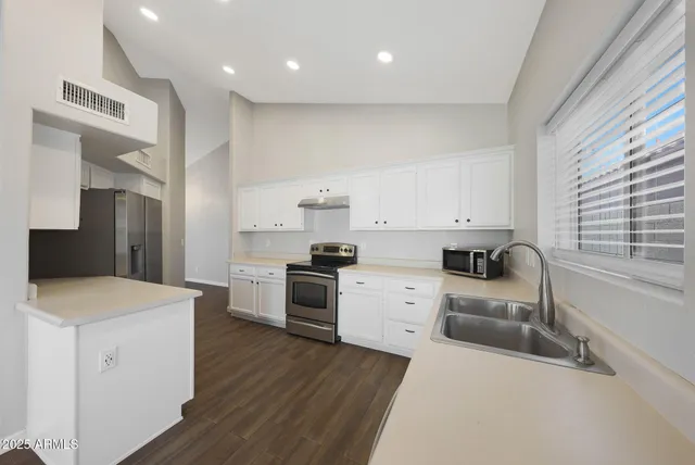 a kitchen with a stove a sink a refrigerator and white cabinets with wooden floor