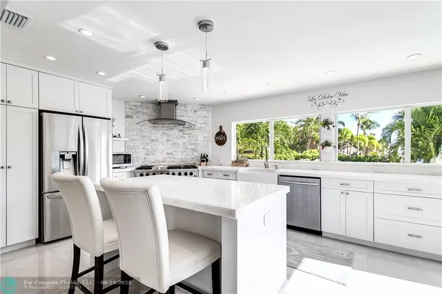 a large kitchen with kitchen island a large window a sink stainless steel appliances and cabinets