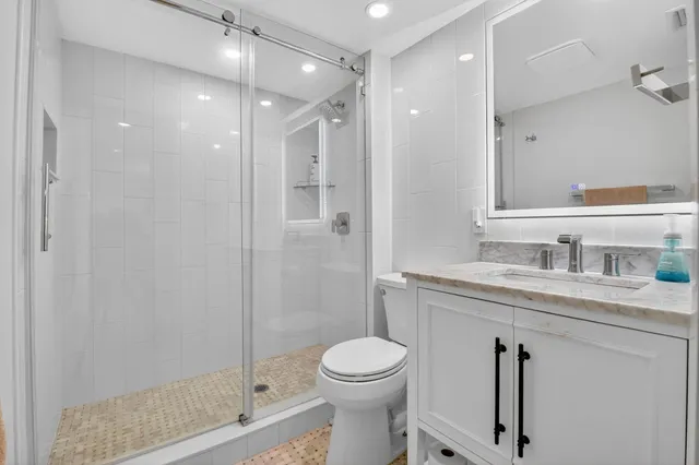 a bathroom with a granite countertop sink a toilet a mirror and shower