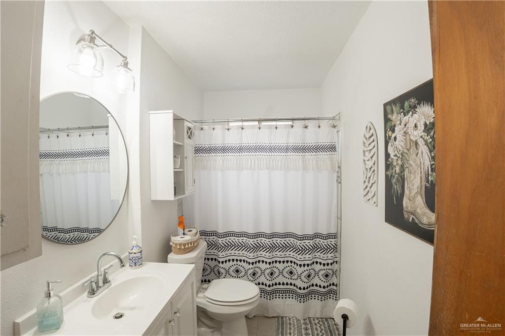 425 South Reynolds Rio Hondo, TX 78583 - Photo 13 of 23 Bathroom featuring a white vanity with a sink, a round mirror, and a shower with a patterned curtain