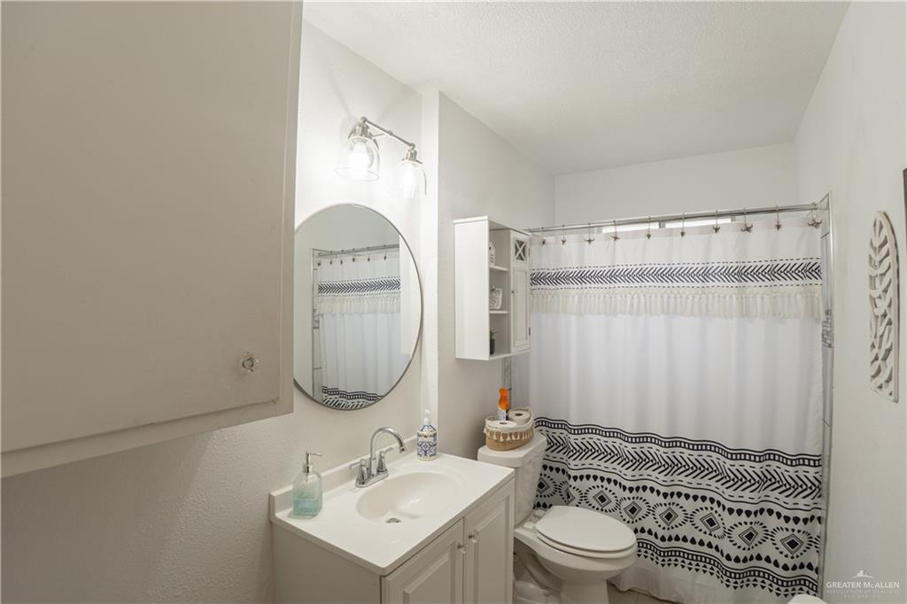 425 South Reynolds Rio Hondo, TX 78583 - Photo 14 of 23 Bathroom with a vanity featuring a white countertop and sink, a round wall mirror, and a wall-mounted light fixture