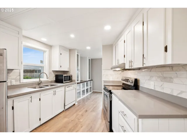 a kitchen with stainless steel appliances kitchen island granite countertop a refrigerator a stove top oven a sink dishwasher and white cabinets with wooden floor