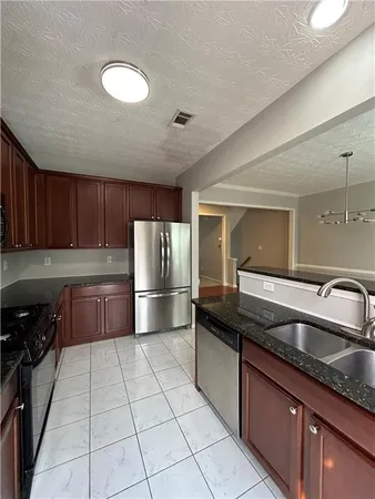 a kitchen with granite countertop a sink a stove top oven a refrigerator and cabinets