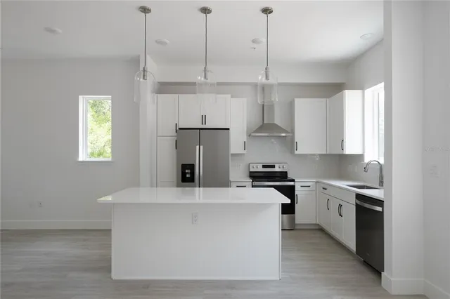 a kitchen with stainless steel appliances a refrigerator a sink dishwasher a stove and white cabinets with wooden floor