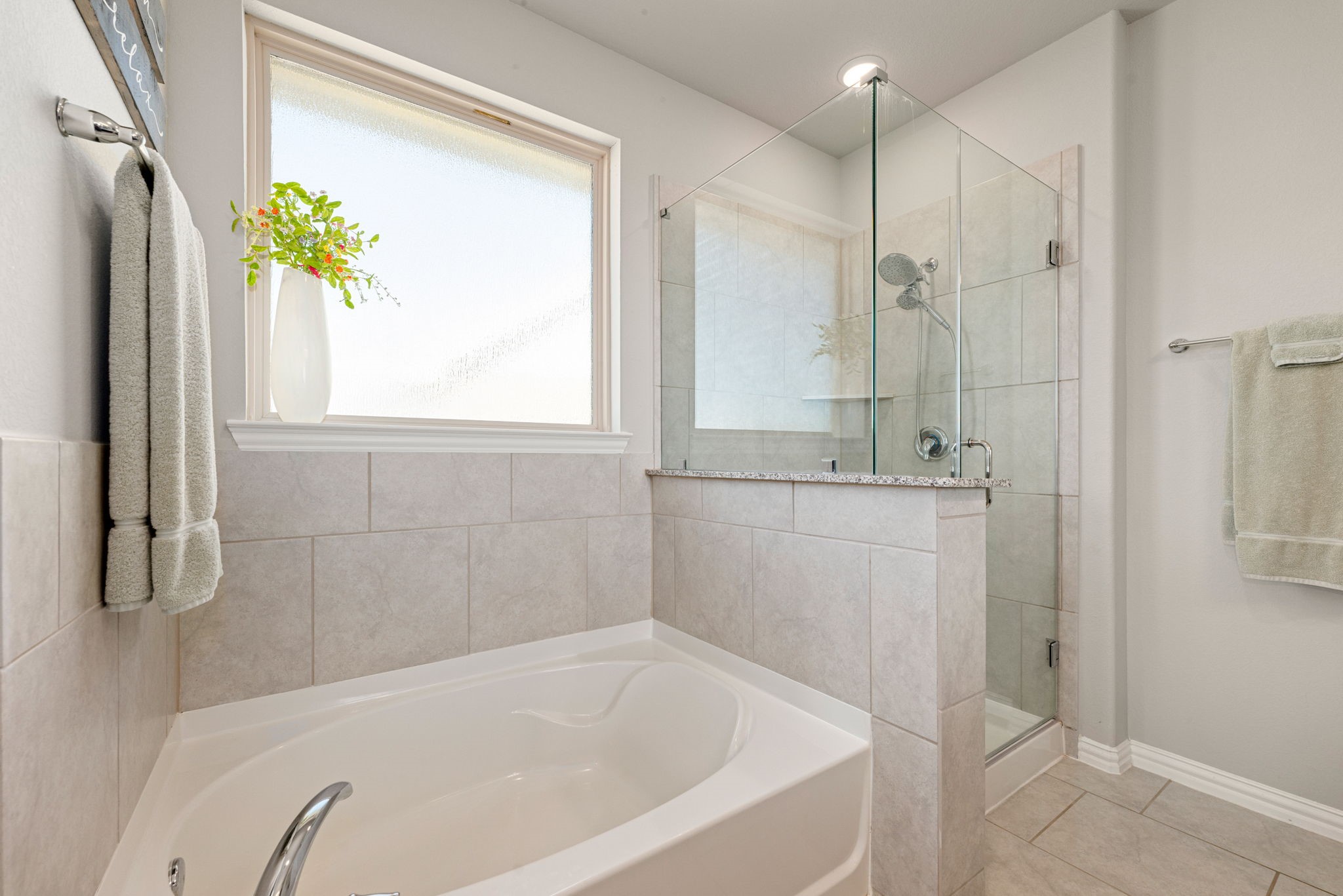 8414 Divot Trace Fulshear, TX 77441 - Photo 15 of 25 This spa-like primary bath retreat features a dedicated soaking tub perfectly positioned under a large window for ample natural light. Adjacent is a modern glass-enclosed walk-in shower with sleek tile surrounds. The space is finished with clean, neutral tones and bright recessed lighting, creating a serene and airy atmosphere.