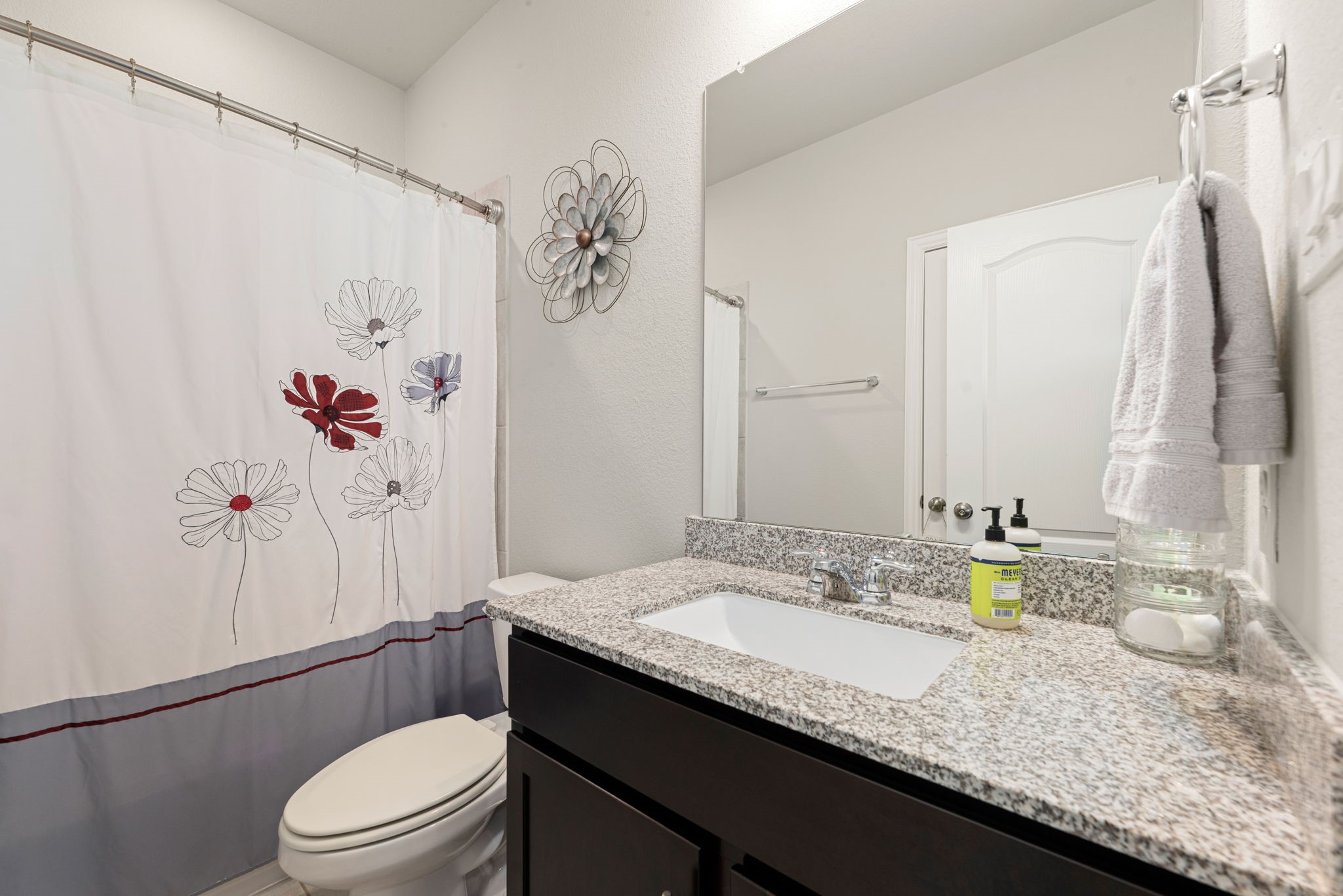 8414 Divot Trace Fulshear, TX 77441 - Photo 20 of 25 This contemporary secondary bathroom features a sleek dark wood vanity topped with a clean white countertop and an undermount sink. The space includes a tub-and-shower combination with a neutral-toned surround and is illuminated by bright wall-mounted sconces. A large vanity mirror and crisp white walls create a refreshed, airy feel throughout.