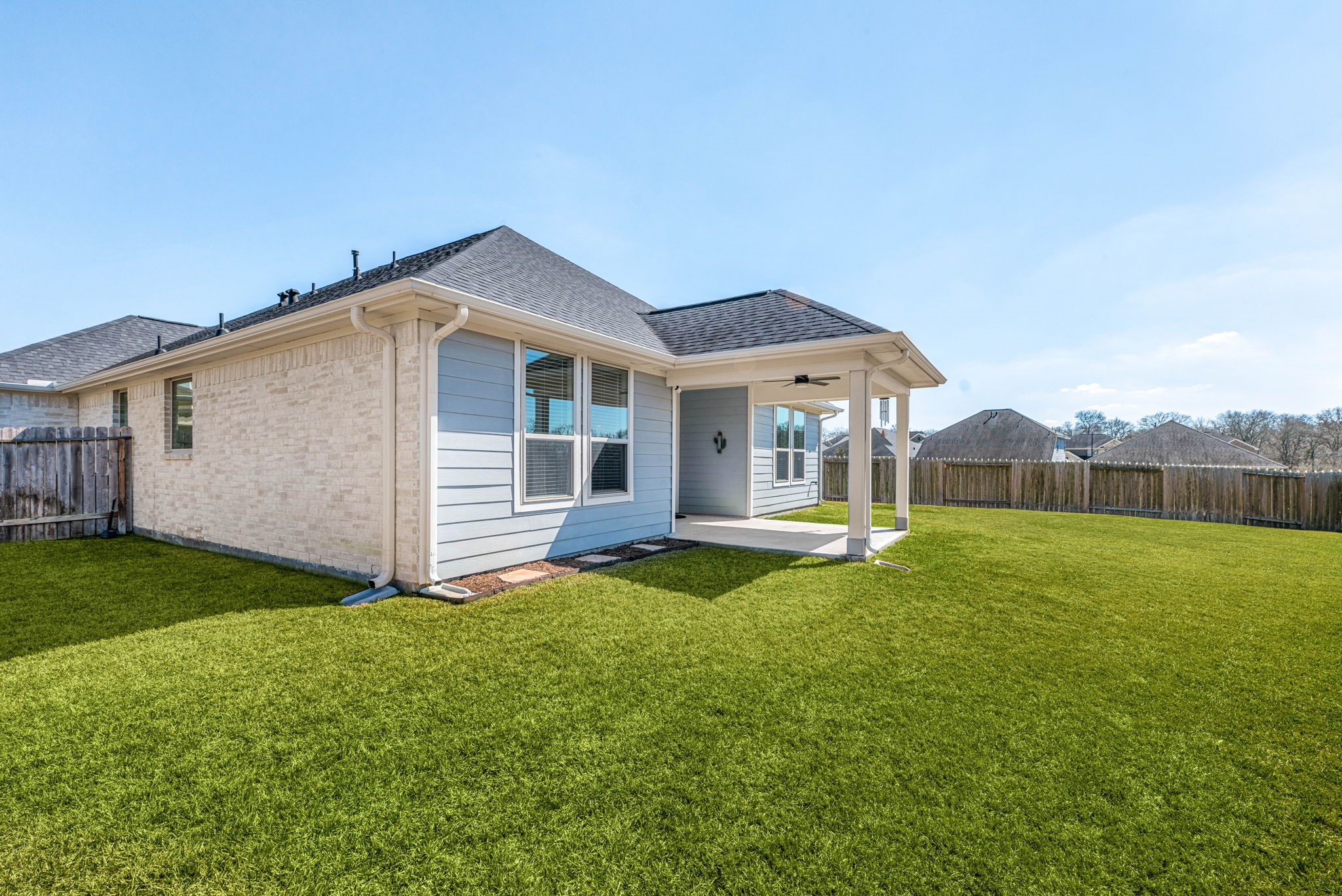 8414 Divot Trace Fulshear, TX 77441 - Photo 21 of 25 This expansive backyard offers a lush, green lawn fully enclosed by a private wood fence. The exterior features a covered patio, perfect for outdoor dining and entertaining, providing a seamless transition from the home to the outdoors. With its clean finish and wide-open space, this backyard is a versatile blank canvas for your dream outdoor oasis.