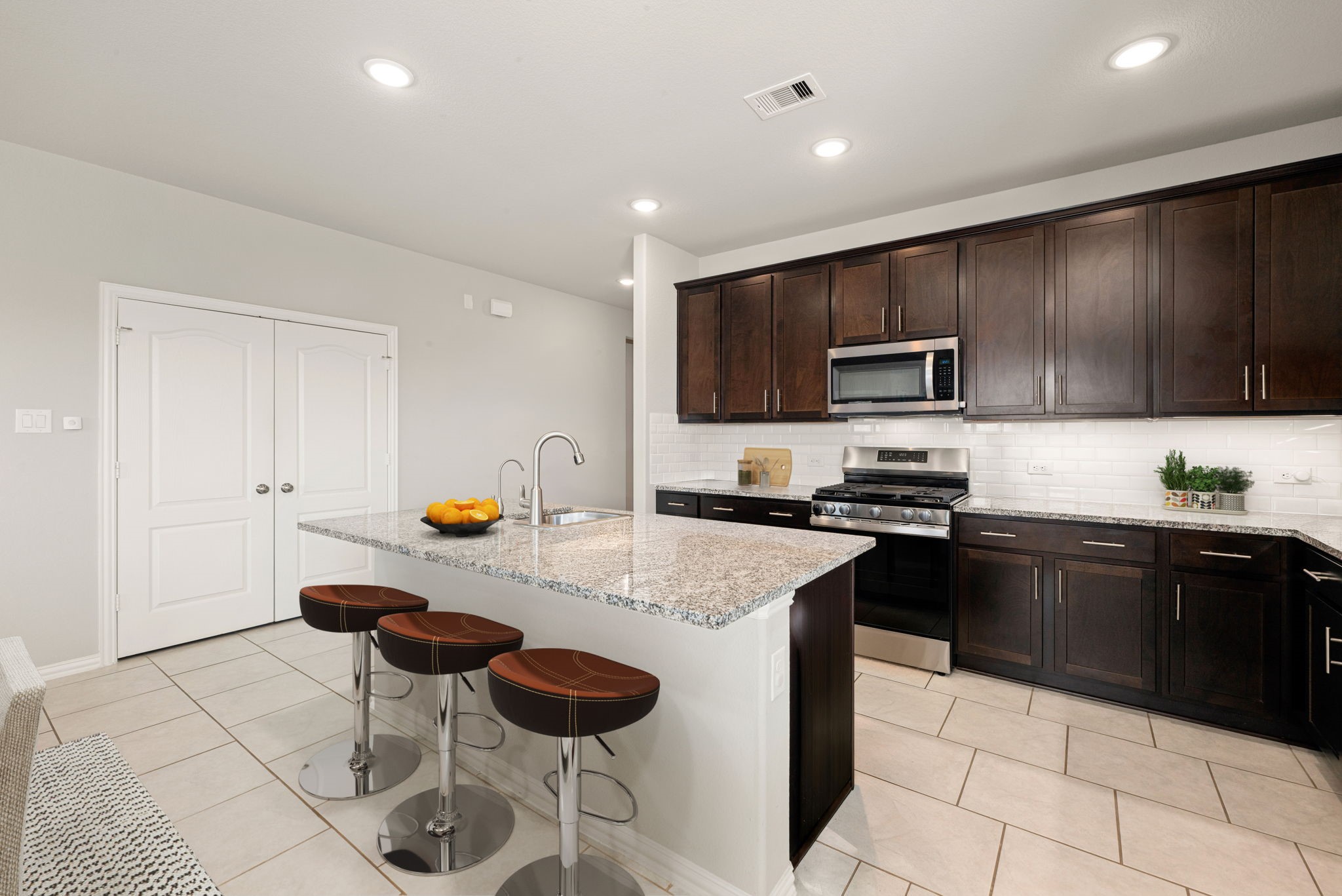 8414 Divot Trace Fulshear, TX 77441 - Photo 7 of 25 This modern, open-concept kitchen features rich espresso cabinetry beautifully contrasted by crisp white countertops and a matching subway tile backsplash. The chef-inspired space is equipped with premium stainless steel appliances, a large center island with a built-in sink, and bright recessed lighting.