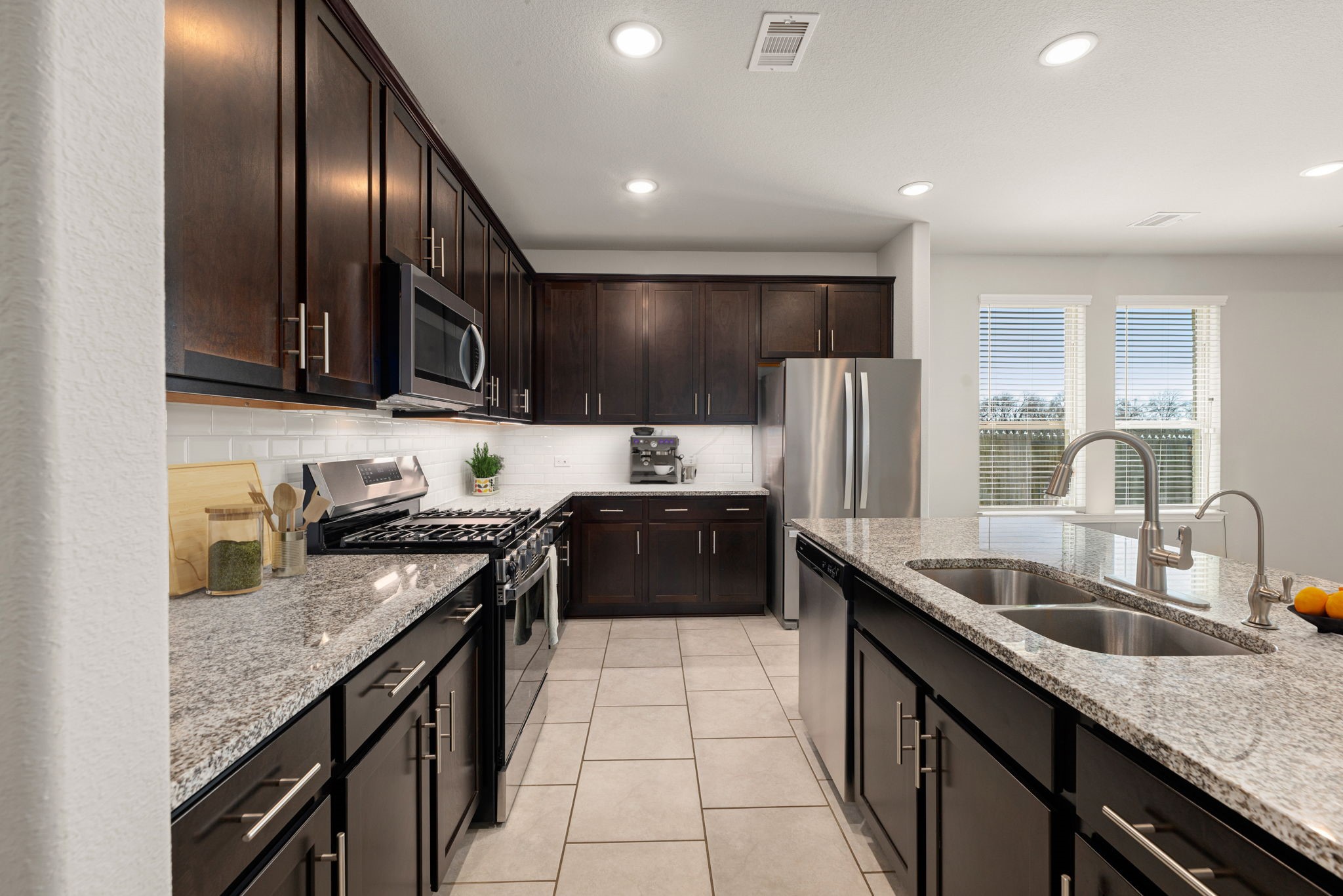 8414 Divot Trace Fulshear, TX 77441 - Photo 8 of 25 This modern, open-concept kitchen features rich espresso cabinetry beautifully contrasted by crisp white countertops and a matching subway tile backsplash. The chef-inspired space is equipped with premium stainless steel appliances, a large center island with a built-in sink, and bright recessed lighting.
