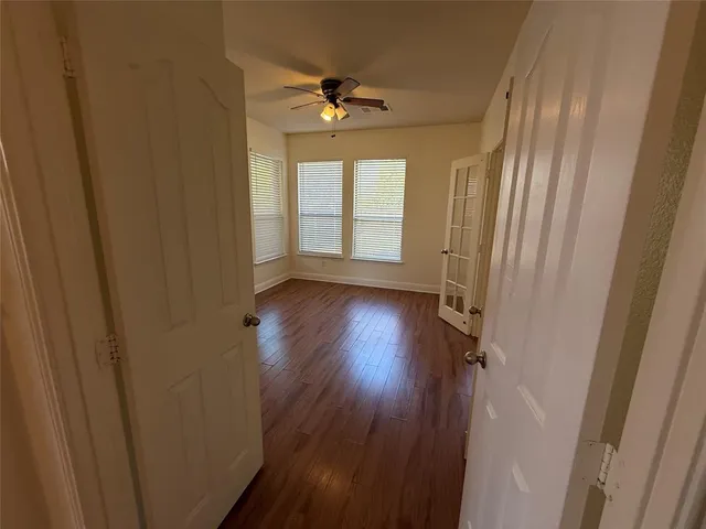 a view of an empty room with wooden floor and a chandelier fan