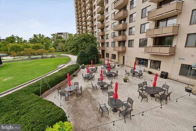 a view of a patio with couches table and chairs under an umbrella with large trees