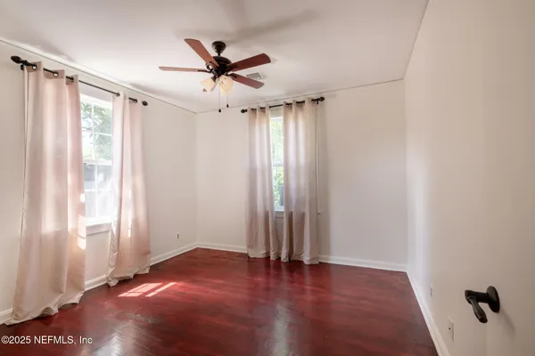 an empty room with wooden floor fan and windows