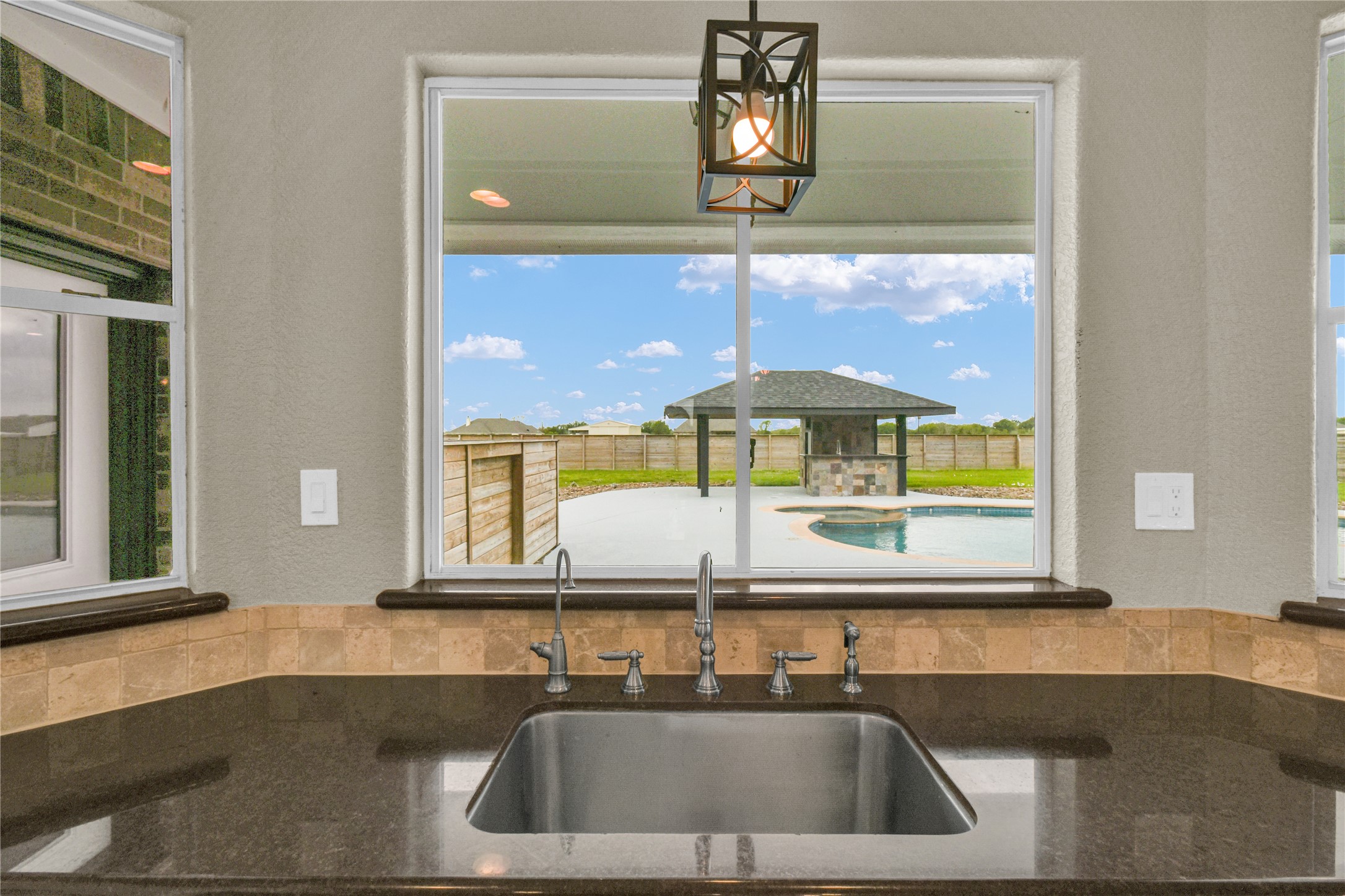 863 Bunkhouse Trail Angleton, TX 77515 - Photo 6 of 22 This photo showcases a kitchen view featuring a sleek, dark countertop with a built-in sink. The large window above the sink offers a picturesque view of the backyard.