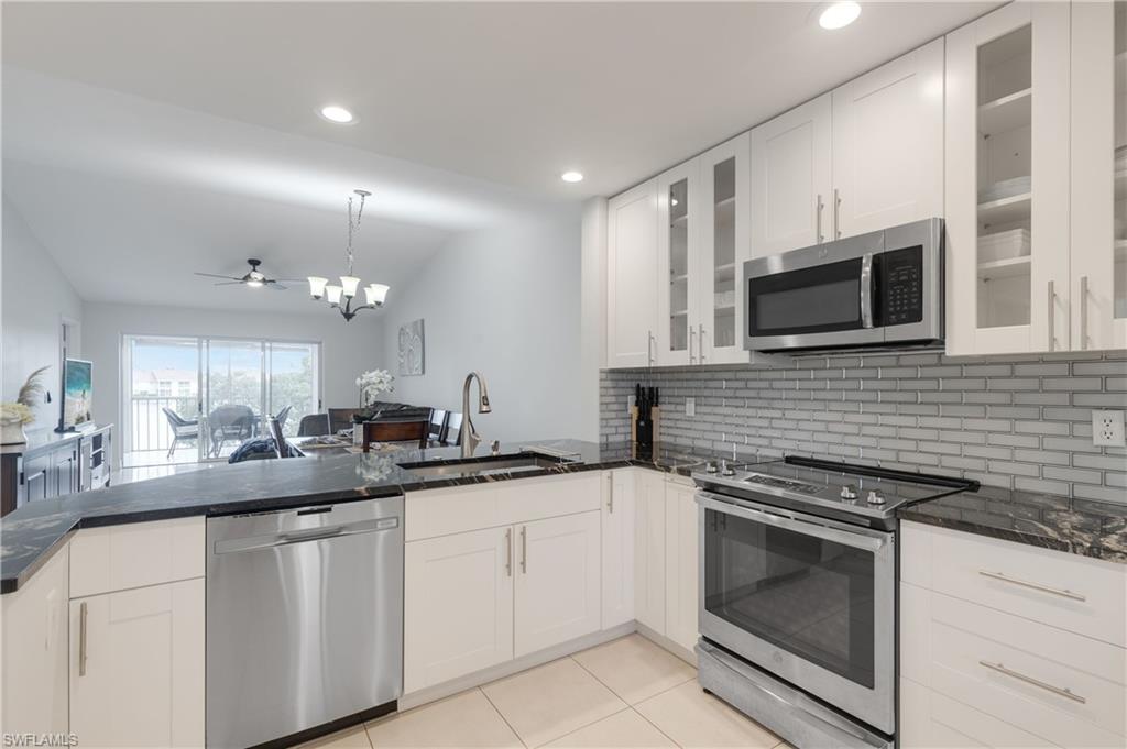 7766 Emerald Circle, Unit R203 Naples, FL 34109 - Photo 3 of 30 Kitchen with stainless steel appliances, backsplash, lofted ceiling, dark stone countertops, and a peninsula