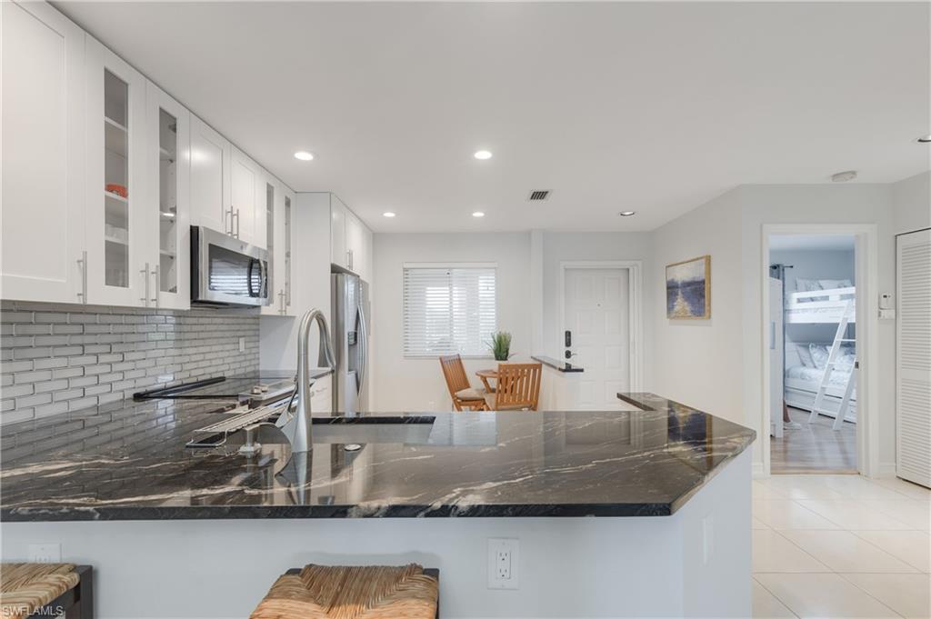 7766 Emerald Circle, Unit R203 Naples, FL 34109 - Photo 9 of 30 Kitchen with backsplash, a peninsula, dark stone counters, stainless steel appliances, and recessed lighting
