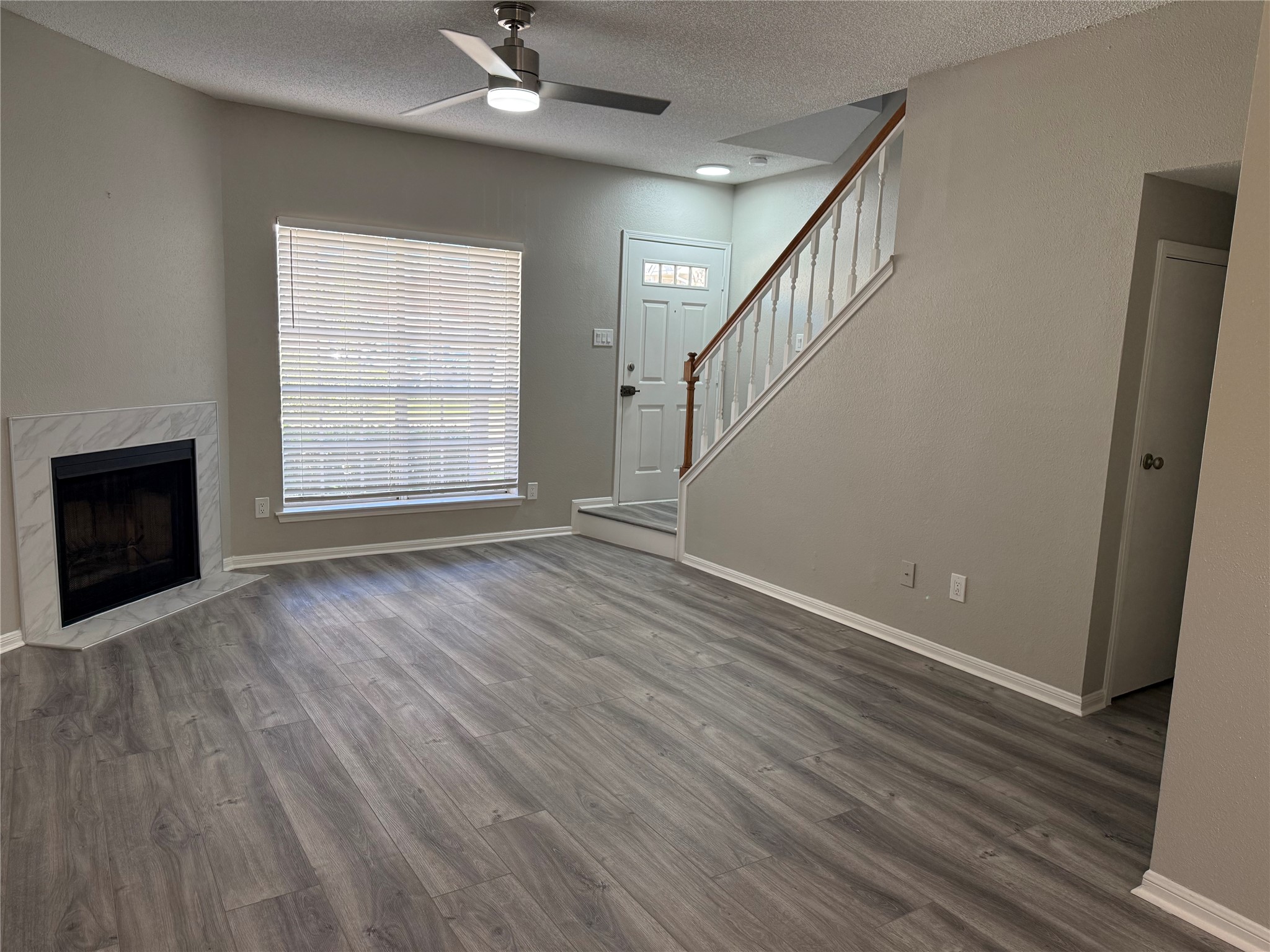 a view of an empty room with wooden floor fireplace and a window