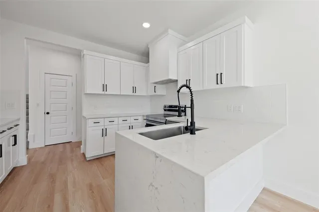 a kitchen with stainless steel appliances a sink dishwasher stove and white cabinets with wooden floor