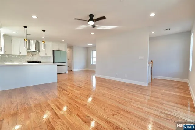 a view of an empty room and kitchen with wooden floor