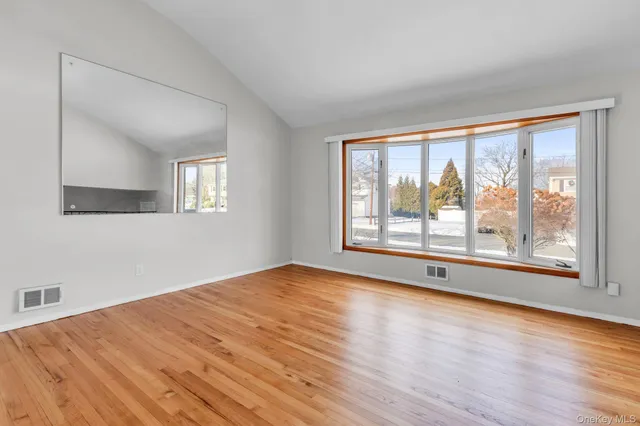 a view of an empty room with a window and wooden floor