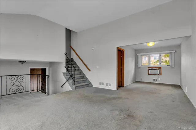 a view of an empty room with stairs and a living room