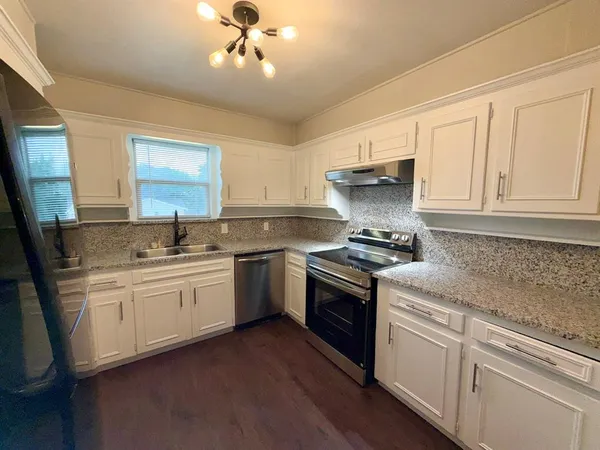 a kitchen with stainless steel appliances kitchen island granite countertop a refrigerator a sink dishwasher a stove and white cabinets with wooden floor