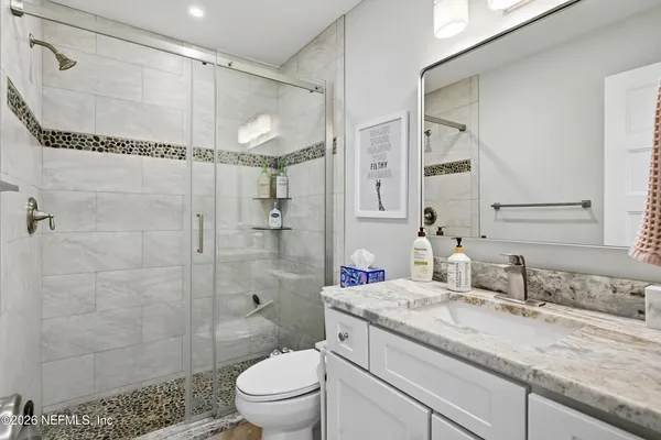 a bathroom with a granite countertop shower sink vanity mirror and toilet