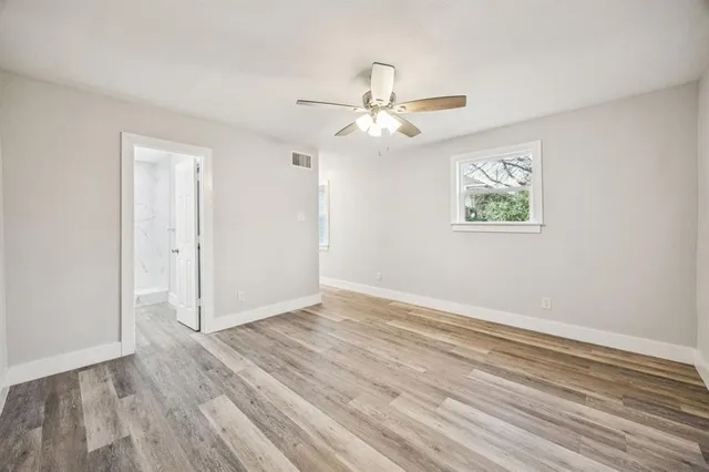 an empty room with wooden floor ceiling fan and windows