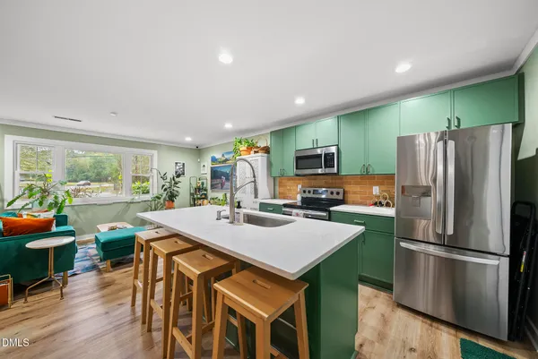 a kitchen with stainless steel appliances a refrigerator a sink a stove a dining table and chairs with wooden floor
