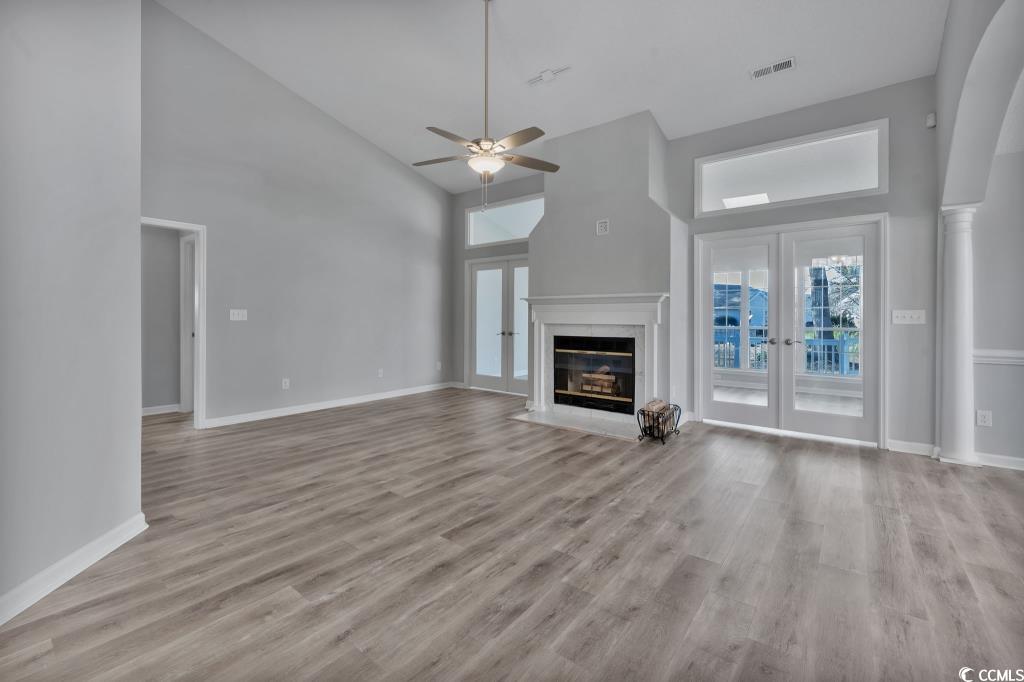 1639 Coventry Road Surfside Beach, SC 29575 - Photo 34 of 38 Unfurnished living room with a towering ceiling, ceiling fan, a premium fireplace, light wood-type flooring, and french doors