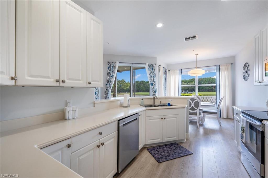 4650 Winged Foot Court, Unit 102 Naples, FL 34112 - Photo 12 of 34 Kitchen featuring stainless steel appliances, a sink, white cabinetry, light wood-type flooring, and a wealth of natural light