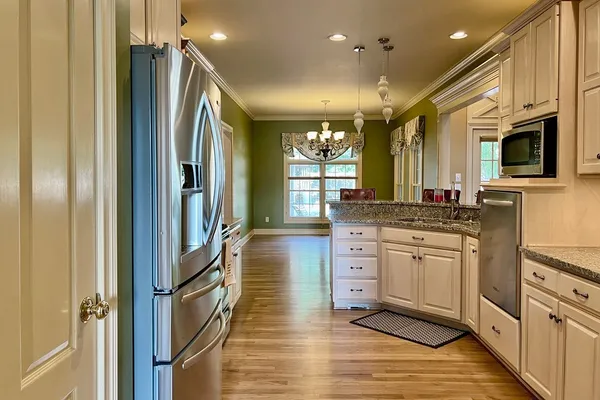 a kitchen with stainless steel appliances granite countertop a refrigerator a oven and white cabinets with wooden floors