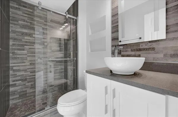 a bathroom with a granite countertop sink a toilet a mirror and shower