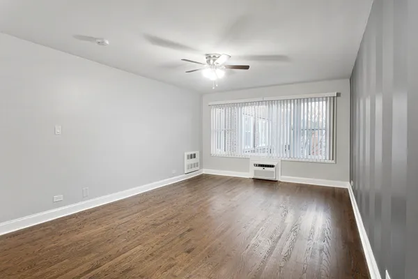 an empty room with wooden floor ceiling fan and windows
