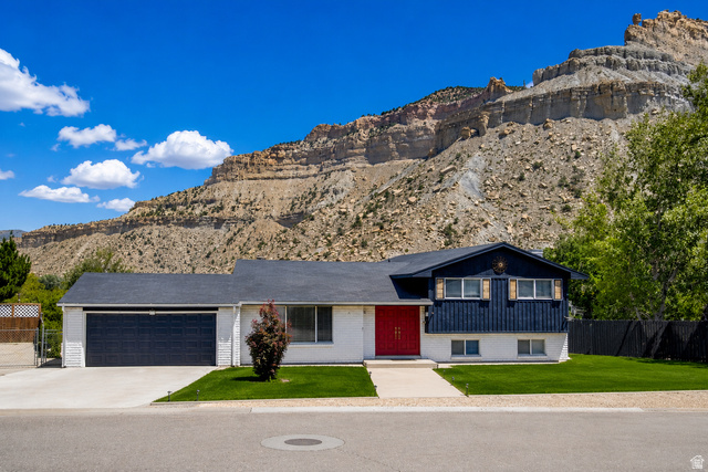 100 Third North Helper, UT 84526 - Photo 2 of 30 Mountain backdrop framing a split-level residence with a red front door, two-car garage, and established front lawn
