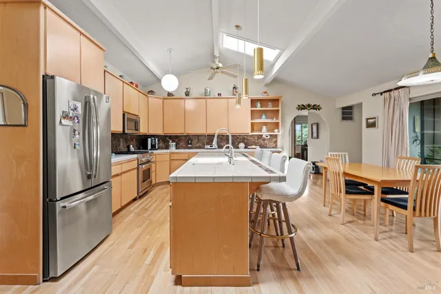 a kitchen with stainless steel appliances a refrigerator a stove a dining table and chairs with wooden floor