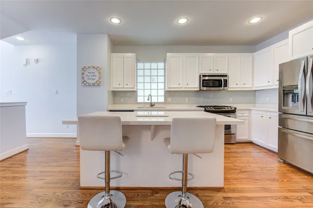 a kitchen with stainless steel appliances granite countertop a stove top oven a sink dishwasher and a refrigerator with wooden floor