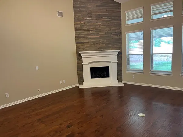 an empty room with wooden floor fireplace and windows