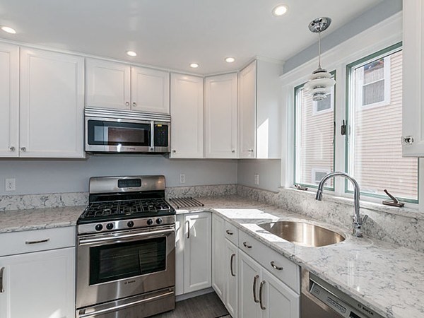 a kitchen with granite countertop a sink white cabinets stainless steel appliances and a window