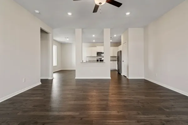 a view of an empty room and kitchen with hardwood floor