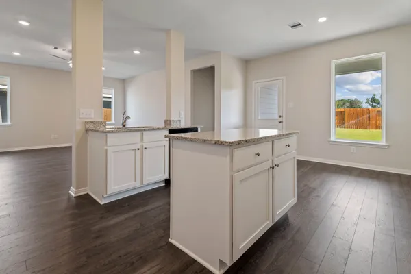 a kitchen with stainless steel appliances granite countertop a dishwasher a stove a sink and white cabinets with wooden floor next to windows