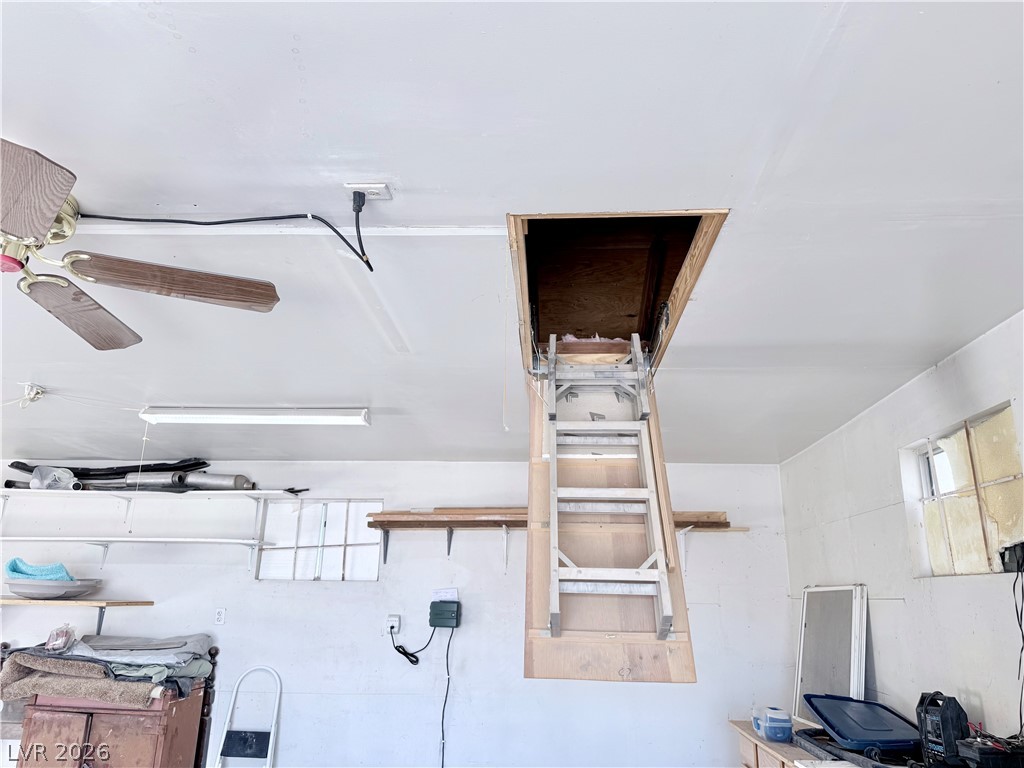 4501 East Kellogg Road Pahrump, NV 89061 - Photo 27 of 52 An interior view of a garage with a ceiling-mounted fan and an attic access ladder.