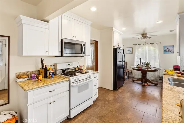 a kitchen with stainless steel appliances kitchen island granite countertop a stove a sink dishwasher and a refrigerator with white cabinets