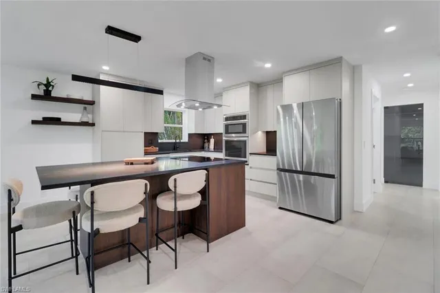 a kitchen with stainless steel appliances a refrigerator a stove a sink and a dining table with white cabinets