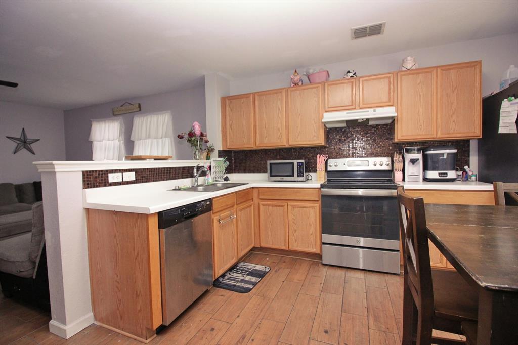 12609 Carpenter Lane Rhome, TX 76078 - Photo 23 of 29 Contemporary kitchen featuring wood-finish flooring, stainless steel appliances, light wood-finish cabinetry, white countertops, and a mosaic tile backsplash