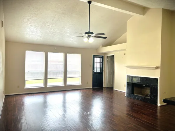 an empty room with wooden floor fireplace and windows