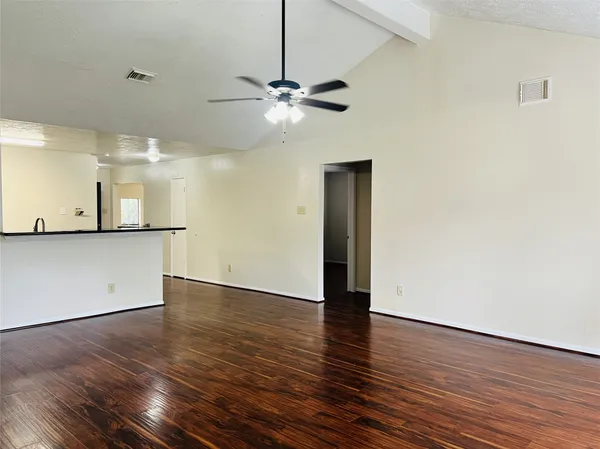 a view of an empty room with wooden floor and a ceiling fan
