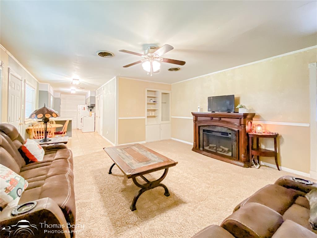 1104 Hickory Street Roscoe, TX 79545 - Photo 8 of 22 Carpeted living area featuring built in shelves, a glass covered fireplace, ceiling fan, and crown molding